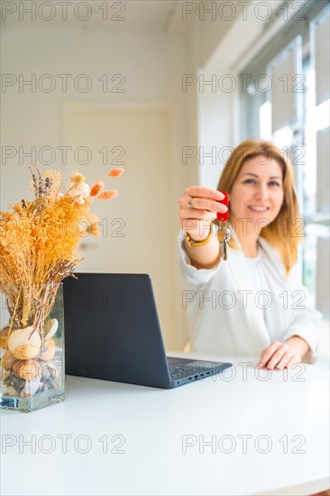 Vertical photo of an elegant female real estate agent delivering the keys of a house at the office