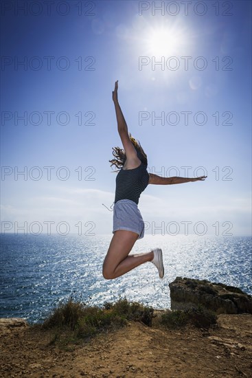 Happy young woman on summer holiday, jump, jumping, jumping, young, glad, happy, luck, joy, emotion, hair, fun, joie de vivre, sun, summer, summer holiday, holiday happiness, tourism, travel, symbolic, symbol, beach holiday, freedom, feeling of freedom, vigour, fit, healthy, health, vital, fitness, authentic, self-confident, self-confidence, Algarve, Portugal, Europe