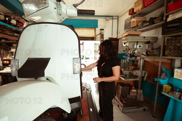 Side view of a mechanic doing precision work on a vintage scooter, latino female in traditional masculine jobs concept, feminine power in real life