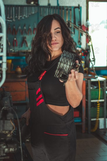 Hispanic Woman with mechanical part in hand, concentrating on her work in a workshop, a complete tool panel in background with bokeh effect, traditional male jobs by Mixed-race female lady