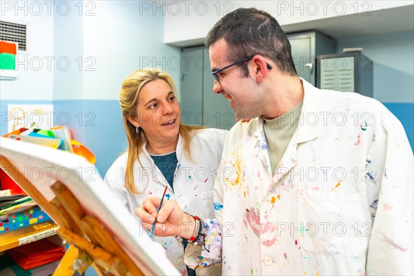 Teacher of a painting class talking to a disabled student in a center of people with special needs