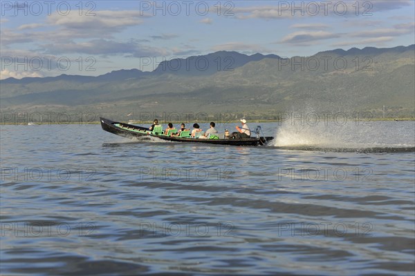 Motorboat with passengers racing on a calm river with mountain backdrop, Inle Lake, Myanmar, Asia