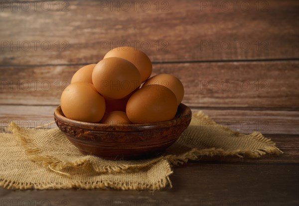 Fresh eggs in a wooden bowl on a burlap cloth on a wooden table