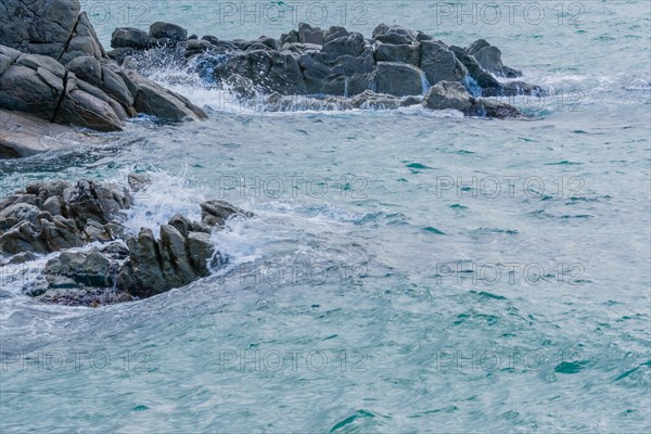 Foamy waves splashing against a rugged coastal rock formation, in South Korea