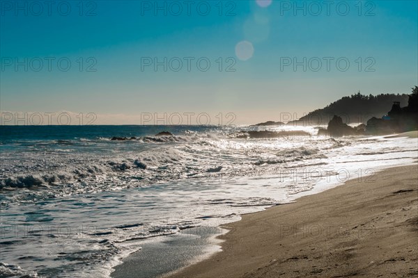 Rugged seascape with waves under bright morning sun crash onto beach and rocks under a beautiful blue sky, in South Korea