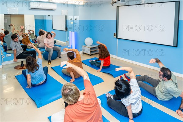 Elevated rear view of a group of male and female disabled people stretching during yoga class together