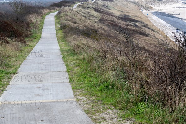 A straight path leads through a hilly dune landscape under a cloudy sky