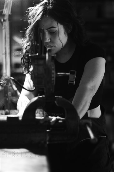 Hispanic latino long haired brunette sexy woman mechanic examining a car part in a well-equipped workshop, a complete tool panel in the out of focus background with bokeh effect