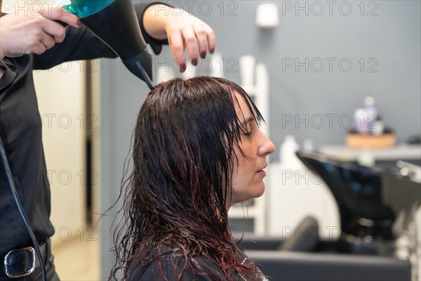 Close-up of the hands of a hairdresser using dryer to dry the hair of a woman in the salon