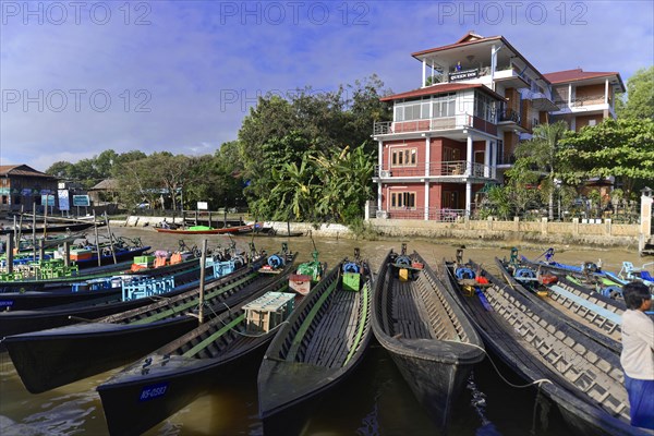 Moored boats on the bank of a river with a large building in the background, Inle Lake, Myanmar, Asia