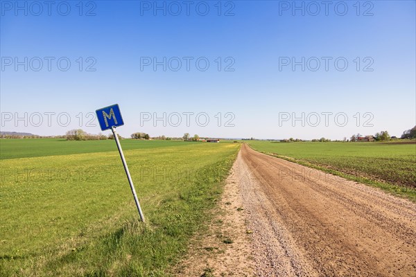 Long straight dirt road in the countryside towards the horizon with a meeting place sign at the roadside a sunny spring day, Sweden, Europe