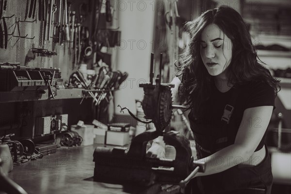 Craftswoman focused on a task at her workbench amid various tools, real women performing traditional man jobs of the past, black and white photograph