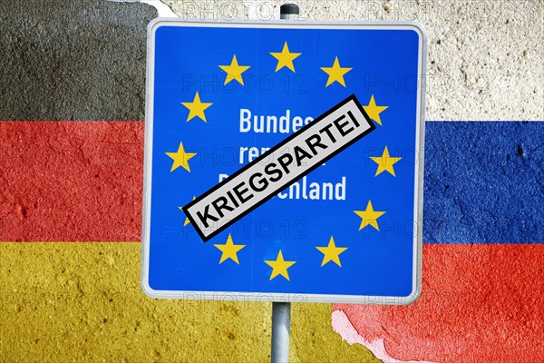 Symbolic image of Germany as a war party: German border sign with the inscription KRIEGSPARTEI in front of the German and Russian flags on a cracked background (Composing)