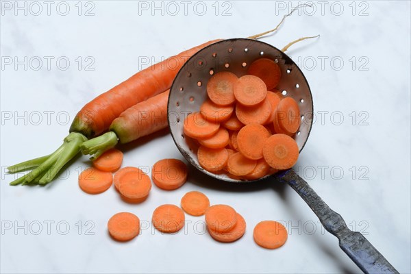 Carrot slices in colander and wooden spoon, Daucus carota