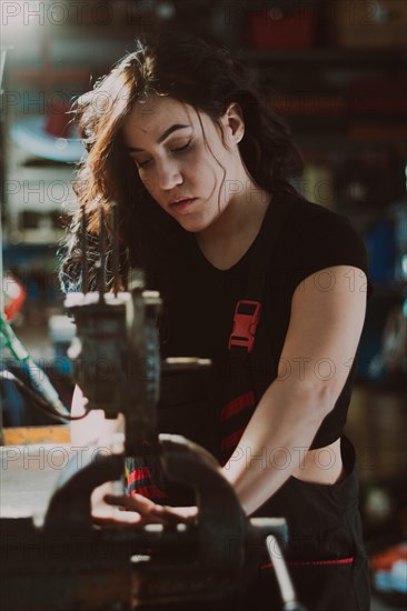 Female technician in the midst of workshop activity, skillfully fixing a component with focus, a complete tool panel in background with bokeh effect, traditional male jobs by Mixed-race latino woman