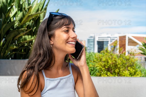 A woman is sitting on a couch and talking on her cell phone. She is smiling and she is enjoying her conversation
