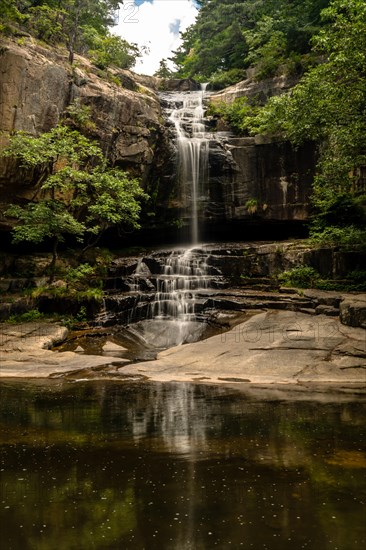 Gentle waterfall with its reflection visible in the clear, still water below, encased by forest, in South Korea