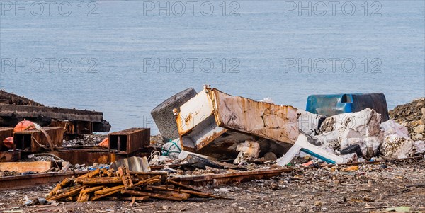 Old rusted metal refrigerator along with other trash and debris laying on the ground with the ocean in the background in an abandoned shipyard in Namhae, South Korea, Asia
