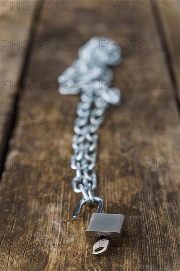 Shiny chain with padlock unlocked on a wooden table in a park with a selective focus
