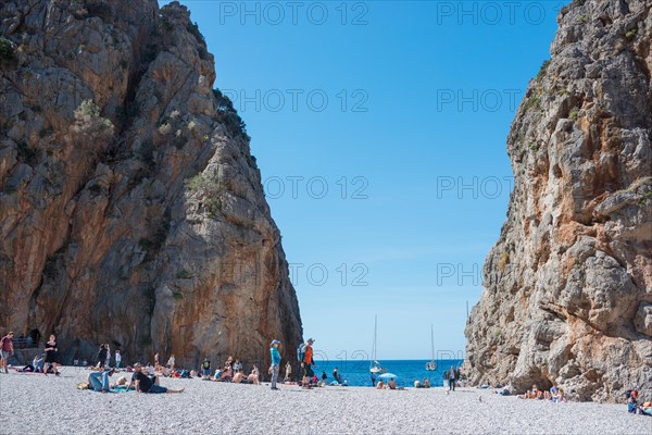 Torrent de Pareis, people relaxing on a popular tourist beach of pebbles framed by high cliffs, sight, cliffs, calm blue sea under a blue cloudless sky with anchored sailboats, yachts, sea, Mediterranean, Serra de Tramuntana gorge, Mediterranean Sea, Majorca Island, Spain, Europe