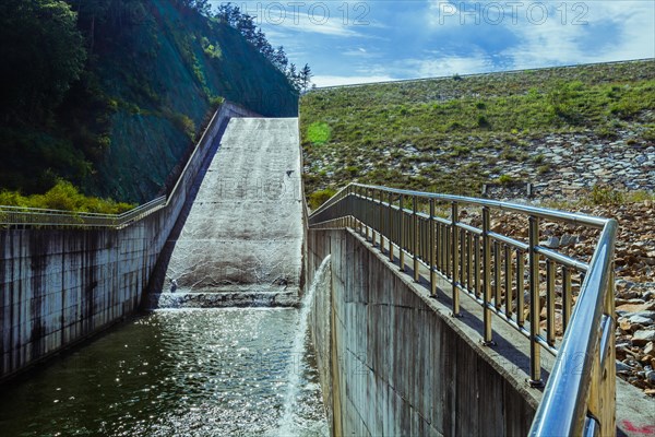 Dam with a sheet of water flowing over its edge, surrounded by mountains, in South Korea