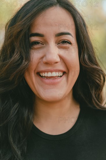 A joyfulCheerful hispanic young woman laughing heartily outdoors with her teeth visible, exuding happiness, selective focus, blurred background with bokeh, daytime, AI generated