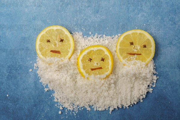 Lemon slices with cloves and cinnamon forming a smiley face on a pile of salt and blue background with copy space
