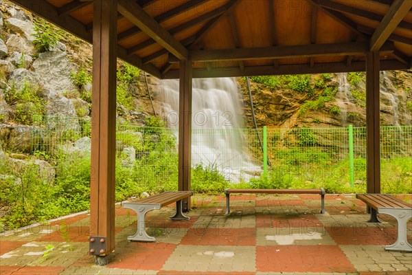 A serene sheltered pavilion with benches overlooking a waterfall, in South Korea