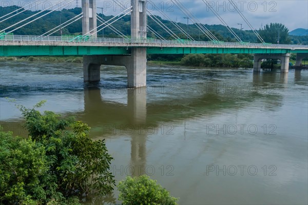 Cloudy atmosphere over a flooded river with trees and bridge infrastructure visible, in South Korea
