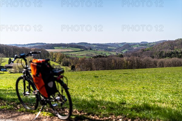 Packed bicycle in front of picturesque spring landscape with green meadows and blue sky, Deilbachtal, Langenberg, Velbert, Mettmann, Bergisches Land, North Rhine-Westphalia