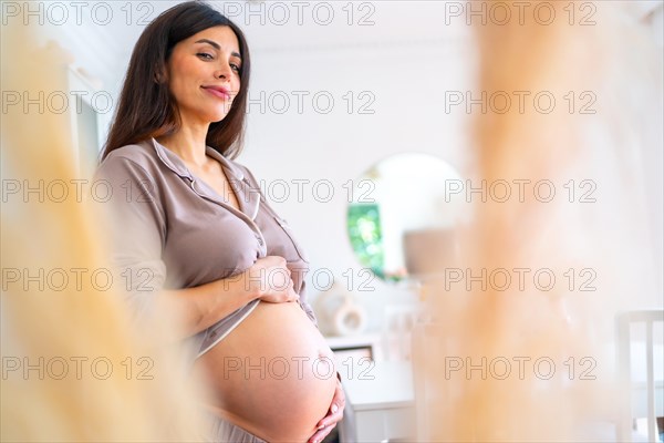 Comfortable beauty pregnant woman standing touching her belly at home