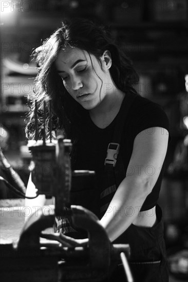 Hispanic latino long haired brunette sexy woman mechanic examining a car part in a well-equipped workshop, a complete tool panel in the out of focus background with bokeh effect