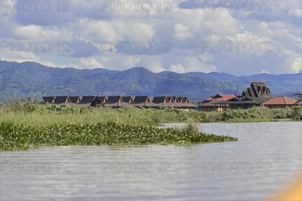 Tranquil river landscape with traditional huts against a mountain backdrop, Inle Lake, Myanmar, Asia