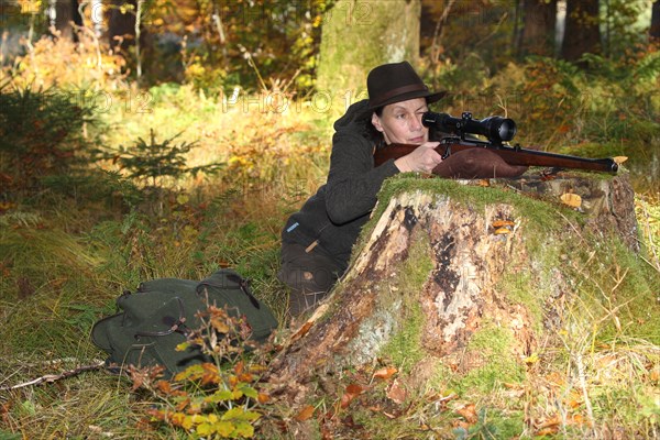 Huntress aims rifle with scope in colourful autumn forest, Allgaeu, Bavaria, Germany, Europe