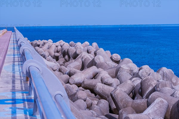 Concrete tetrapods line a coastal walkway under clear skies, with a vivid blue ocean in the background, in South Korea
