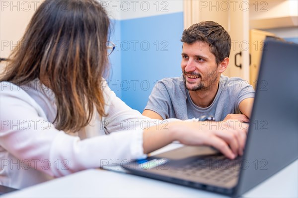 Teacher helping a disabled woman using laptop during IT class in a day center for people with special needs