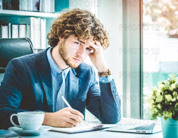 Thoughtful, young man works in a bright office at a desk with laptop, AI generated, AI generated