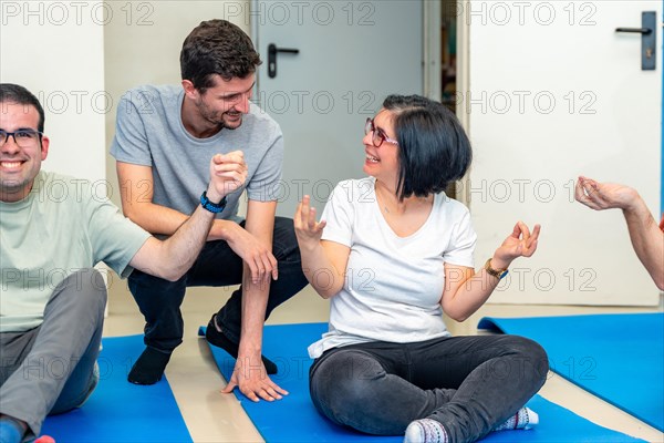 Yoga instructor talking with a happy adult disabled woman sitting on a mat during yoga class