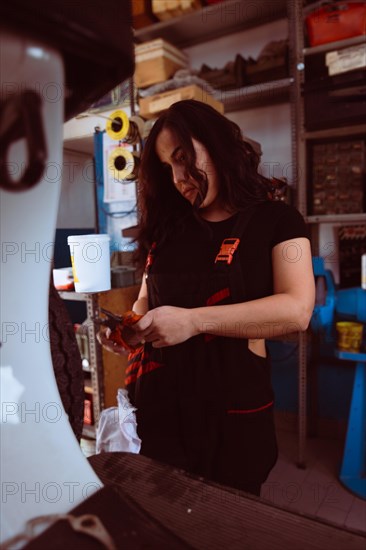 Hispanic young sensual long haired brunette Mechanic with a draper applying detail to a classic scooter, latino female in traditional masculine jobs concept, feminine power in real life