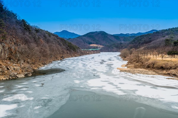 A clear blue sky over a frozen river winding through a winter mountain landscape, in South Korea