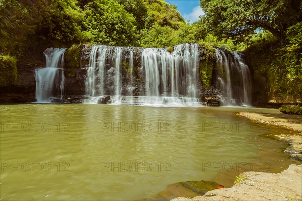 Landscape of a waterfall taken with ND filter with trees and blue sky in the background and water basin in the foreground in Guam