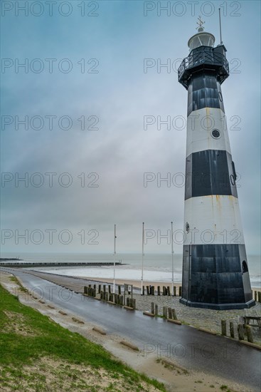 Black and white lighthouse on the coast with grass and sand under a cloudy sky, Breskens, Zeeland, Netherlands