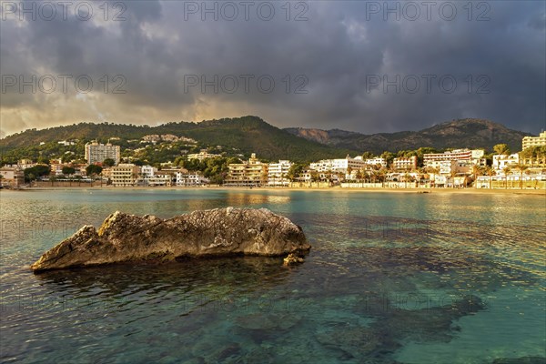 Coastal town by the sea at sunset with golden clouds and a large rock in the water, Peguera, Mallorca