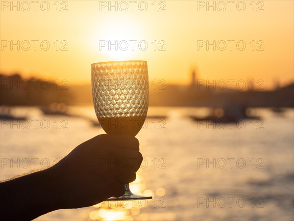Tourist holding wine glass against the light, sunset over the town of Rab, island of Rab, Kvarner Gulf Bay, Croatia, Europe