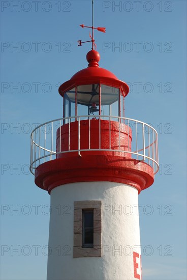 Red and white lighthouse against a clear blue sky, symbolizing maritime navigation and safety