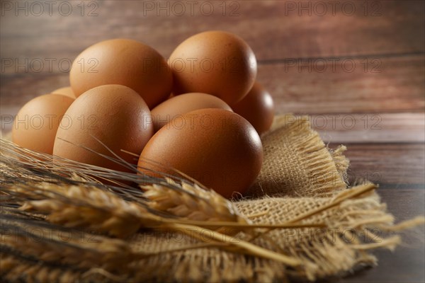 Fresh eggs on a burlap cloth on a wooden table with out-of-focus ears of wheat