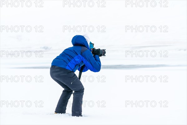 Adventurous photographer woman in winter in Iceland photographing on a frozen lake below zero