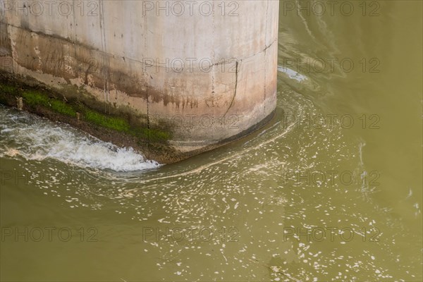 Water swirling around the algae-covered base of a concrete bridge pillar, in South Korea