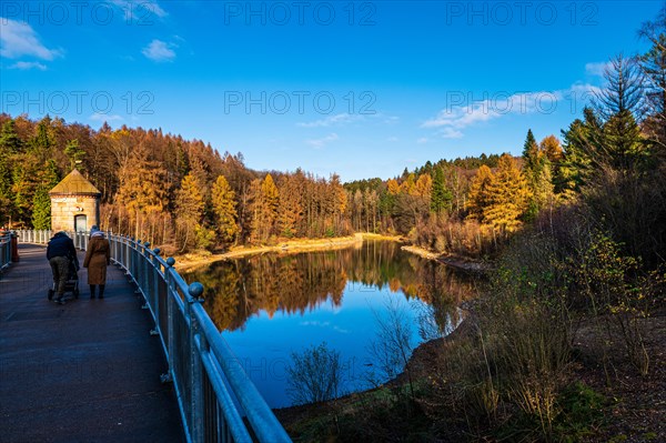 Autumn forest reflected in a dam under a clear blue sky, walkers on the dam wall, Ronsdorfer Talsperre, Ronsdorf, Wuppertal, Bergisches Land, North Rhine-Westphalia