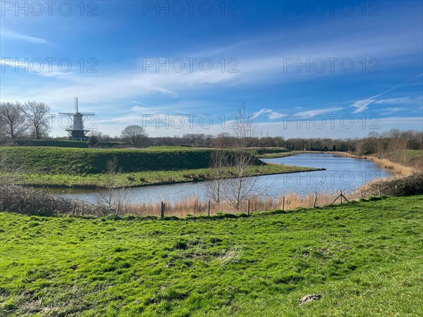 Sunny landscape with a windmill on the riverbank, surrounded by nature